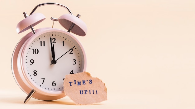 Times up text on torn paper near the alarm clock against beige background