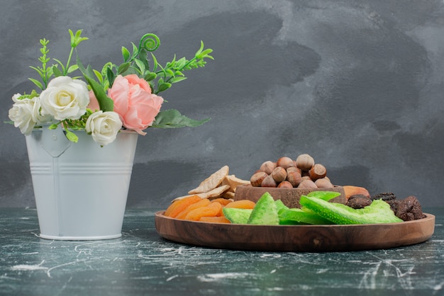 Tiny bouquet with wooden plate of dried fruits on marble wall .