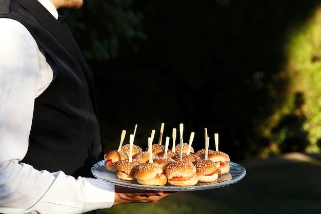 Tiny burgers served on a plate held by the waiter