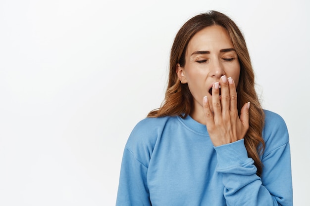 Tired adult woman yawning and covering opened mouth with hand