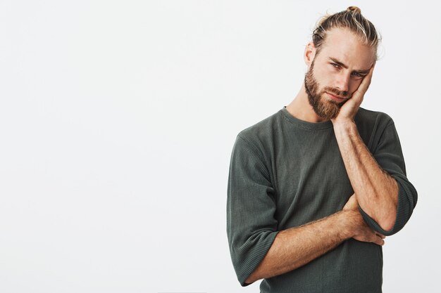 Tired attractive man with stylish hairstyle and beard in grey shirt exhausted looking