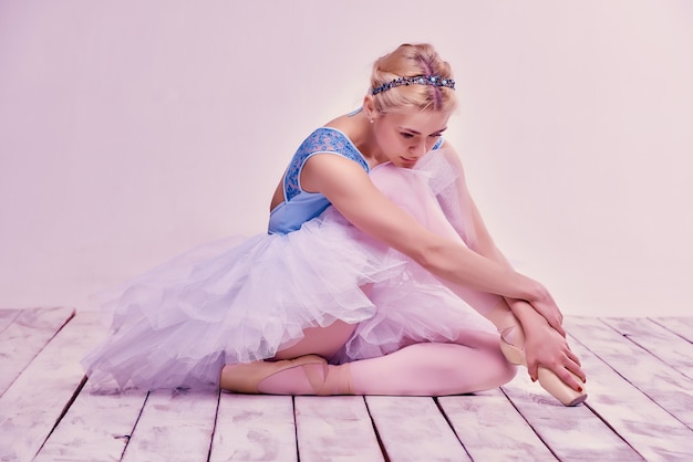 Tired ballet dancer sitting on the wooden floor