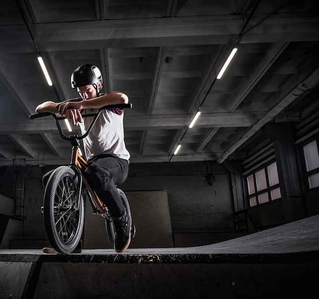 Free photo tired bmx rider in protective helmet sitting on his bicycle in a skatepark indoors