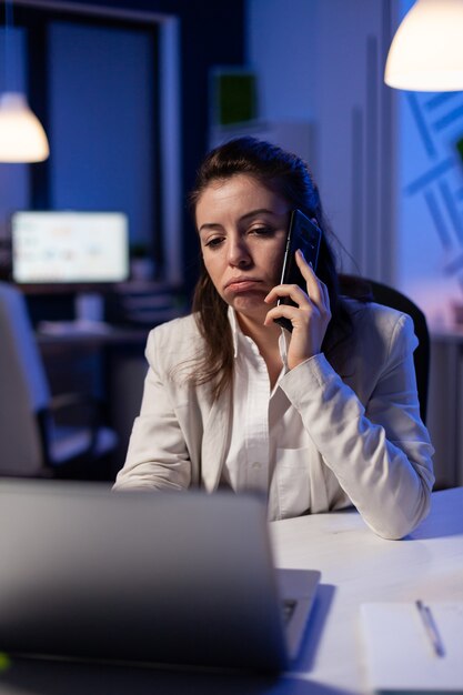 Tired corporate freelancer having conversation on phone while working exhausted for economic statistics in business office late at night Focused employee using modern technology network wireless