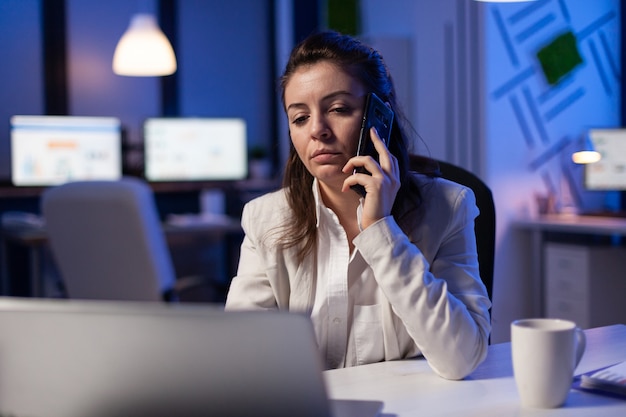 Tired corporate freelancer having conversation on phone while working exhausted for economic statistics