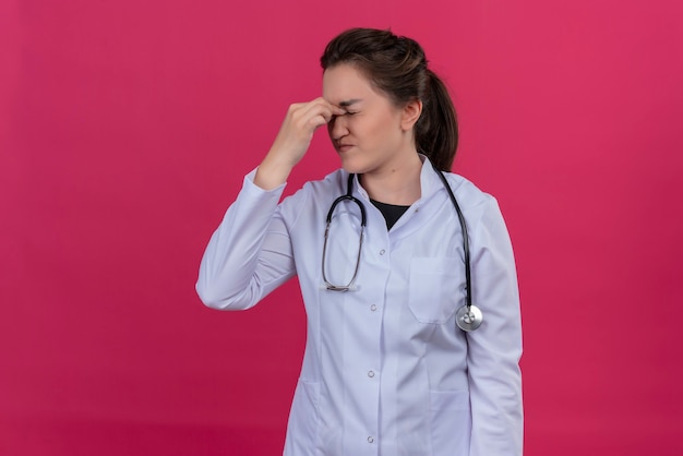 Tired doctor young girl wearing medical gown and stethoscope put her hand on forehead on isoleted red background