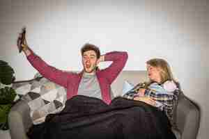 Free photo tired father watching tv while mother with baby sleeping