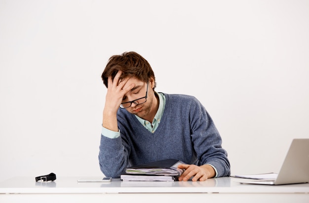 Tired male office worker, sighing uneasy, working late, have deadlines, studying reports and docusments as sit table with laptop, facepalm distressed