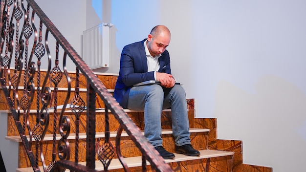 Tired stressed businessman losing concentration on business deadline at workplace closing laptop sighing sitting on stairwell. Corporate entrepreneur doing overtime working in financial building.