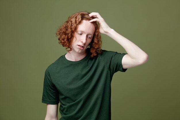 Tired with closed eyes putting hand on head young handsome guy wearing green t shirt isolated on green background