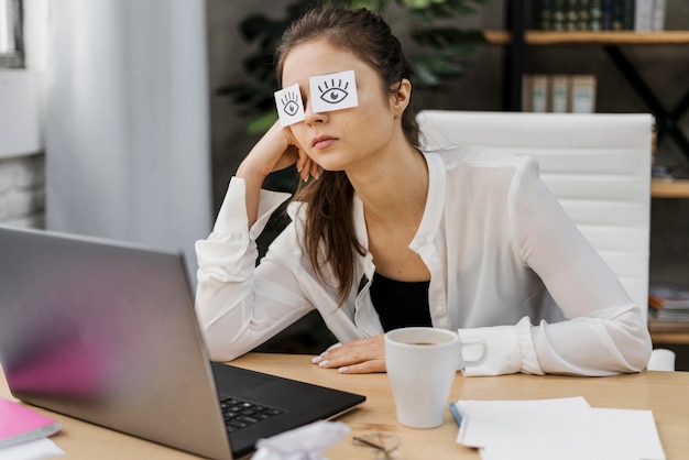 Tired woman covering her eyes with drawn eyes on paper