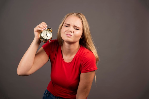 Tired woman holding clock on dark background. High quality photo