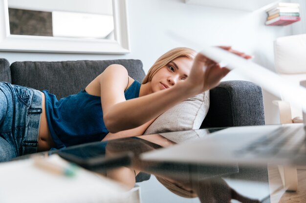 Tired woman lying on sofa and closing laptop at home