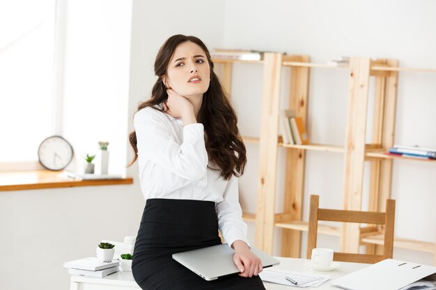 Tired young businesswoman suffering from long time sitting at computer desk in office