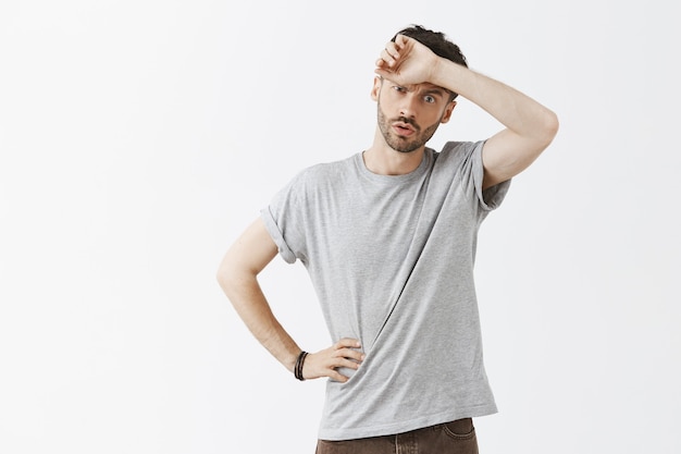 Tired young handsome guy posing against the white wall