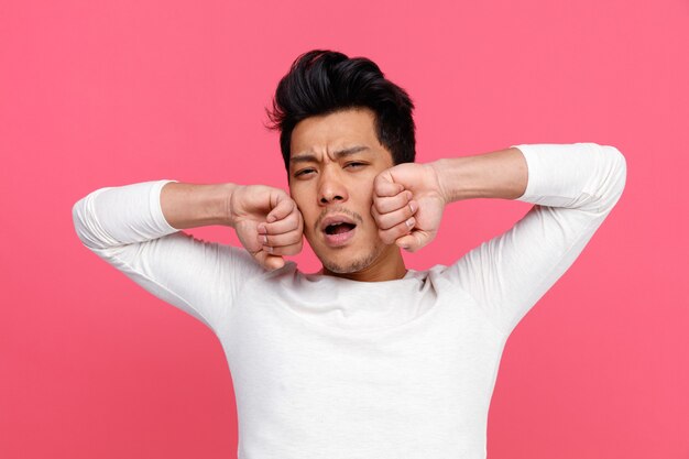 Tired young man yawning touching face with hands stretching 