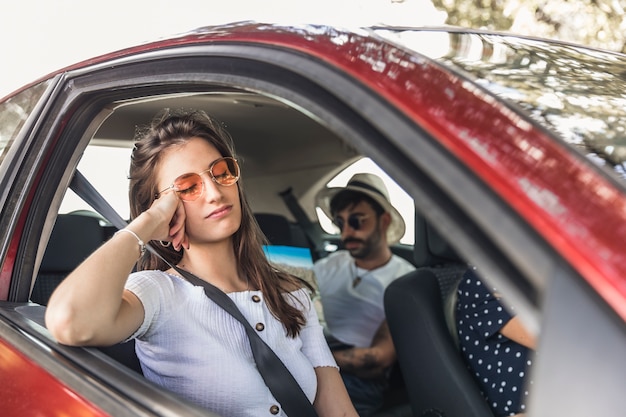 Tired young woman sleeping in car with her friends