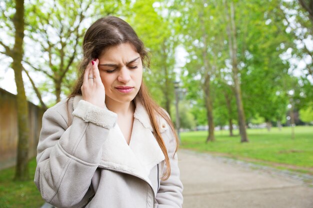 Tired young woman touching temple in park