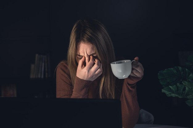 Tired young woman working behind a laptop at night sick eyes