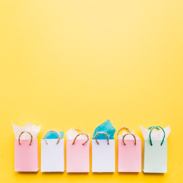 Free photo tissue papers in the row of shopping bags arranged on yellow background