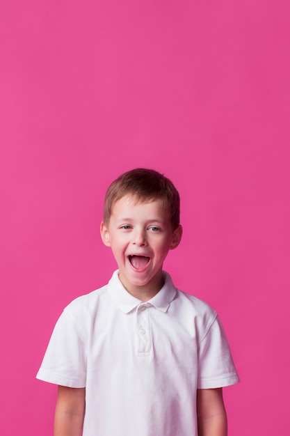 Free photo tittle boy standing near pink wall with mouth open