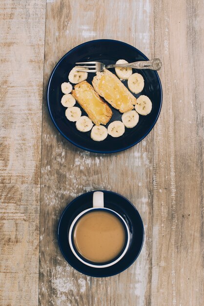 Toast bread and banana slices on plate with coffee cup on wooden table