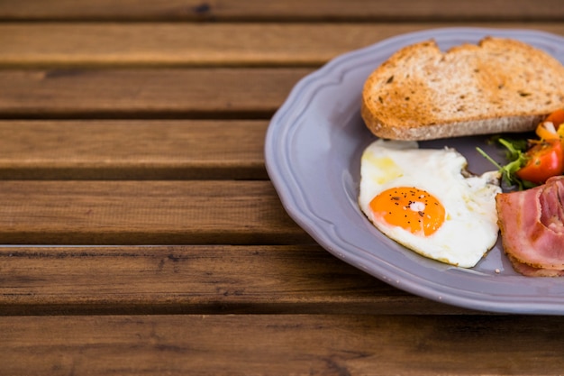 Free photo toast; fried egg; bacon on ceramic gray plate over the wooden table