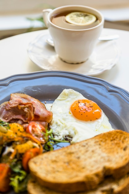 Free Photo toast; half fried egg; salad and bacon on gray plate in front of tea cup over the table