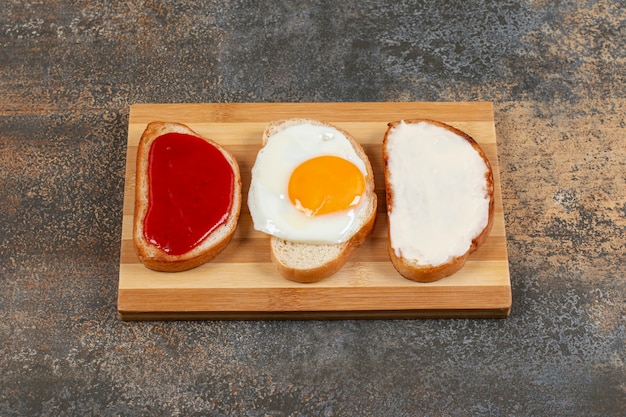 Free photo toast with egg, cream cheese and jam on wooden board.