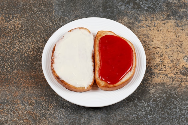 Free photo toasts with strawberry jam and sour cream on white plate.