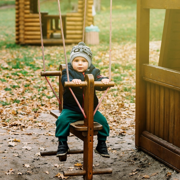 Free photo toddler boy on swing in autumn garden