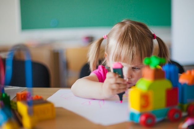 Free photo toddler girl drawing on paper in classroom