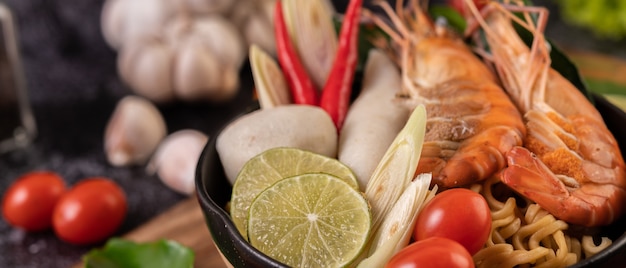 Tom Yum Kung in a bowl with tomato, chili, lemongrass, garlic, lemon, and kaffir lime leaves