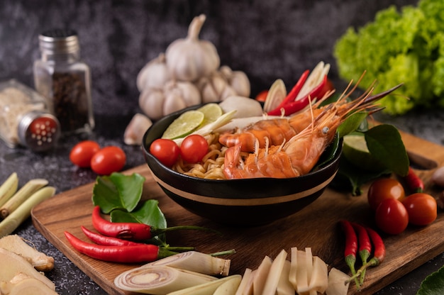 Tom Yum Kung in a bowl with tomato, chili, lemongrass, garlic, lemon, and kaffir lime leaves