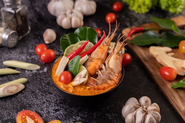 Tom Yum Kung in a bowl with tomato, chili, lemongrass, garlic, lemon, and kaffir lime leaves