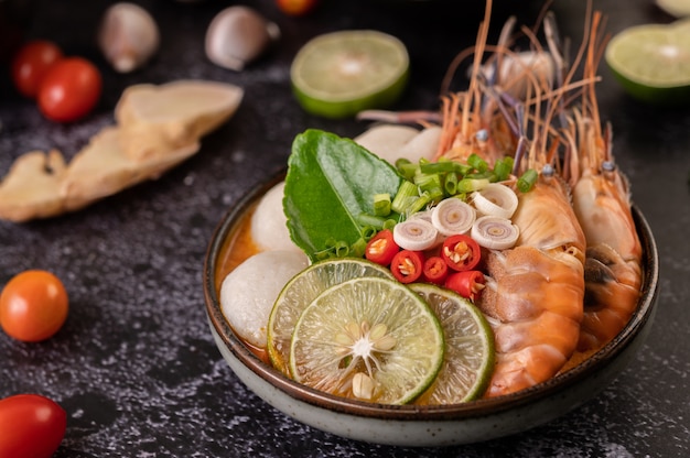 Tom Yum Kung in a bowl with tomato, chili, lemongrass, garlic, lemon, and kaffir lime leaves