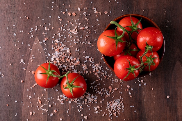 tomato in ceramic bowl with salt top view on wooden table