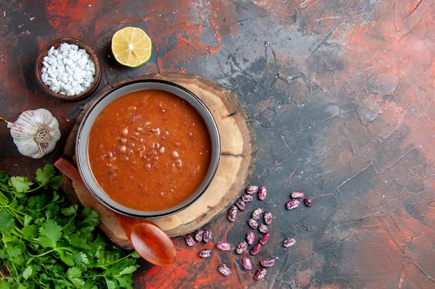 Free photo tomato soup in a blue bowl spoon on wooden tray garlic salt and lemon a bunch of green on mixed color table footage