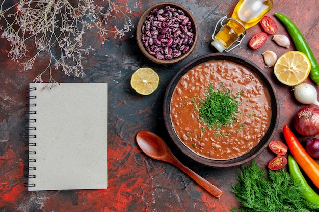 Free photo tomato soup oil bottle beans lemon a bunch of green and notebook on mixed color table