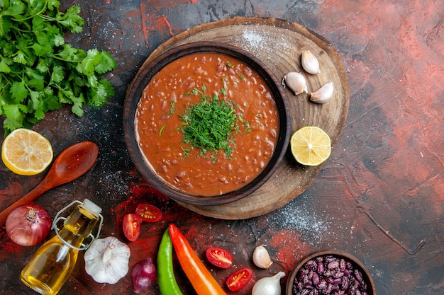 Free photo tomato soup with a bunch of green oil bottle garlic and spoon on mixed color table