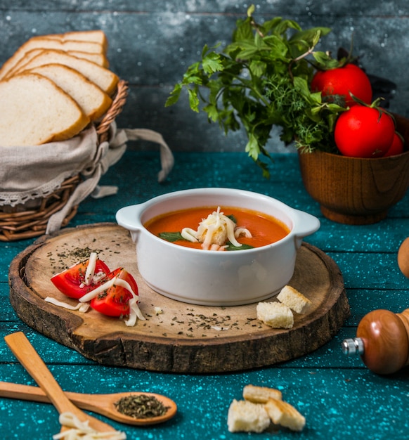 Free photo tomato soup with parmesan on a piece of woode with tomatoes and crackers around.