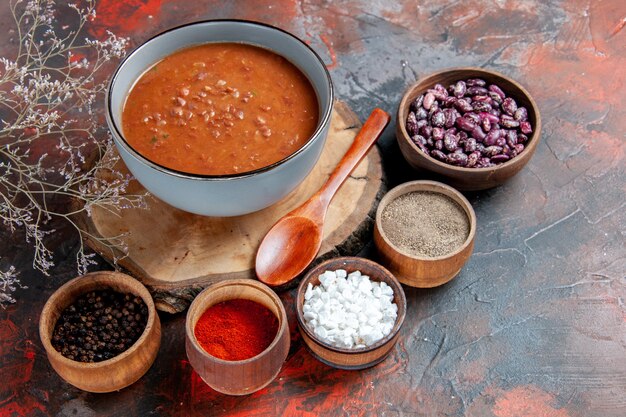 Tomato soup with spoon on wooden tray beans and different spices on mixed color table