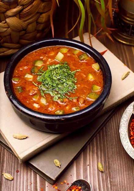 Tomato zucchini vegetable soup with herbs in black bowl on the books