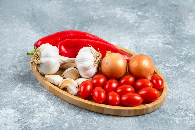 Tomatoes, garlic and peppers on wooden plate. 