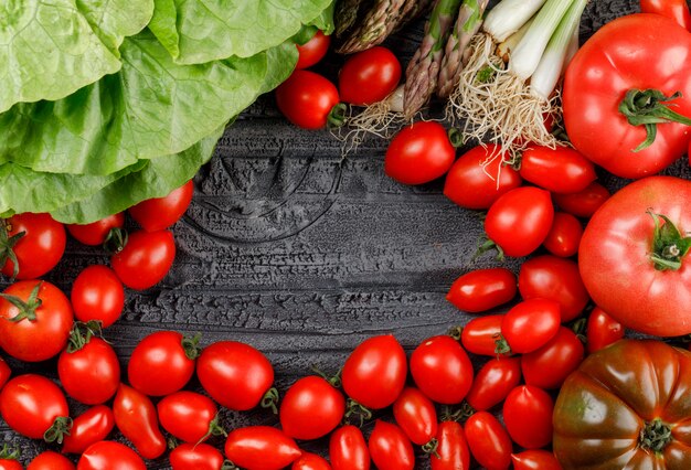 Tomatoes pile with lettuce, asparagus, green onions flat lay on a grey wooden wall