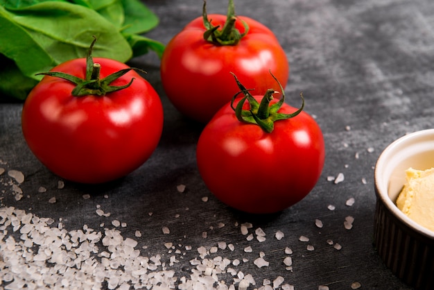 Free photo tomatoes, salt and greens over grey wooden surface