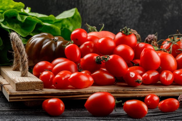 Tomatoes variety in a handmade tray with lettuce side view on wooden and dark wall