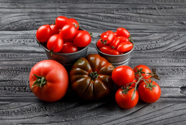 Tomatoes variety in mini buckets on grey wooden wall, high angle view.