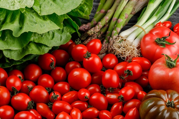 Tomatoes variety with lettuce, asparagus, green onions close-up on a wooden wall