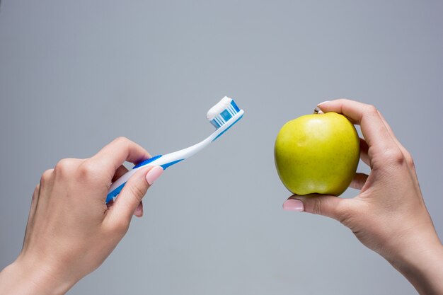 Toothbrush and apple in woman's hands on gray